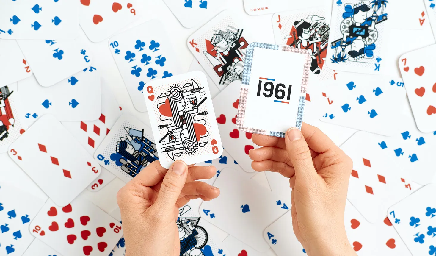 Two hands holding custom playing cards above a pile of scattered playing cards.