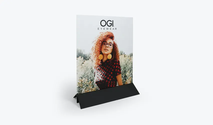 A free-standing sign printed with a woman wearing glasses and OGI and standing in a black base frame.