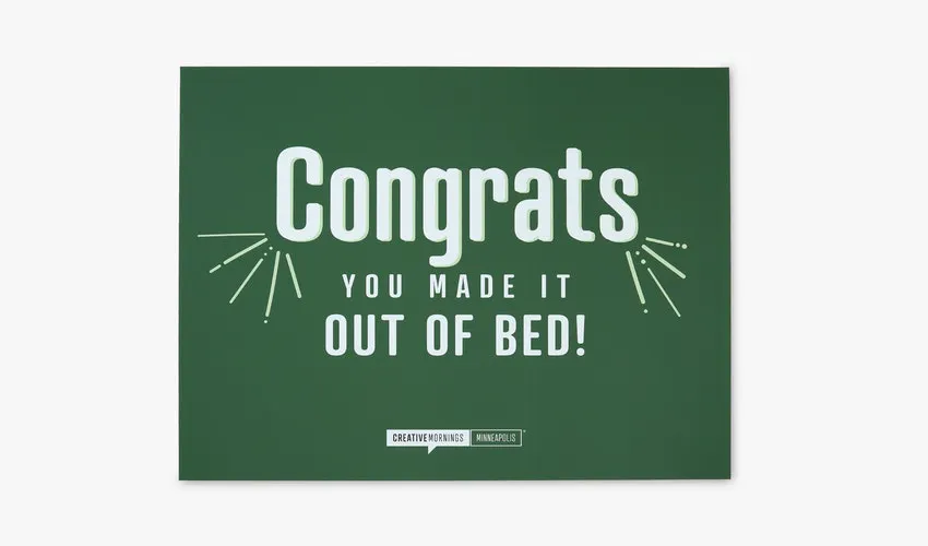 A polystyrene foam sign printed with a green background and Congrats You Made it Out of Bed! in white.