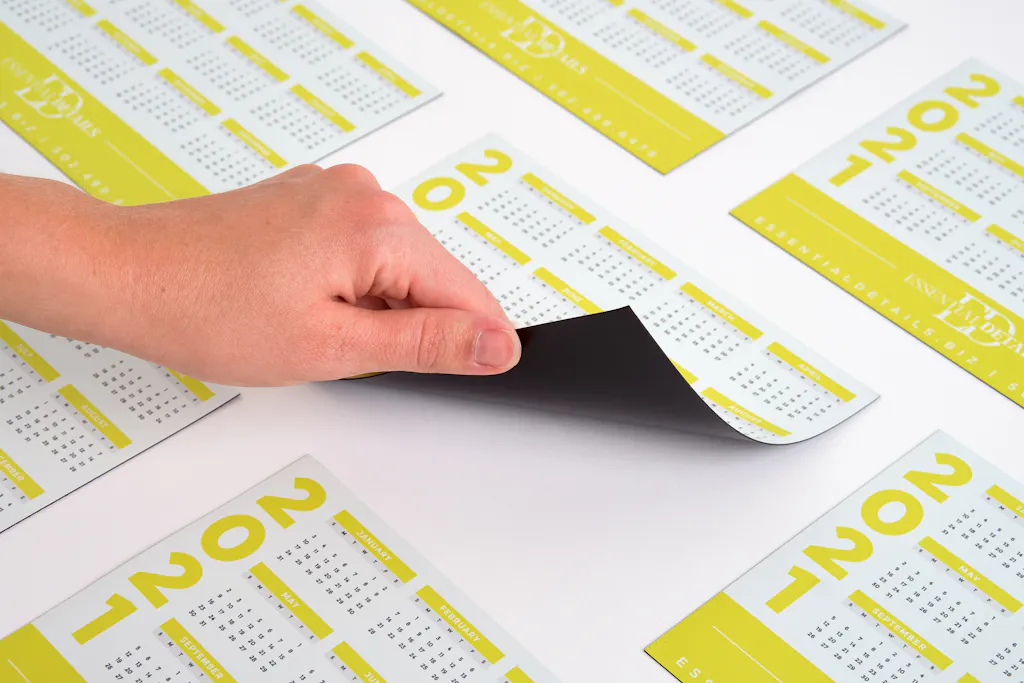 A hand holding up the corner of a magnet calendar printed with 2021 and a white and yellow design.