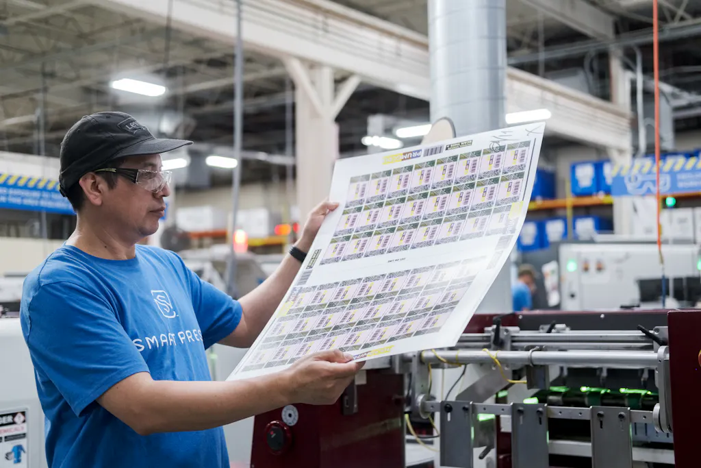 A man in a print production facility holding up a sheet of a repeated designs.