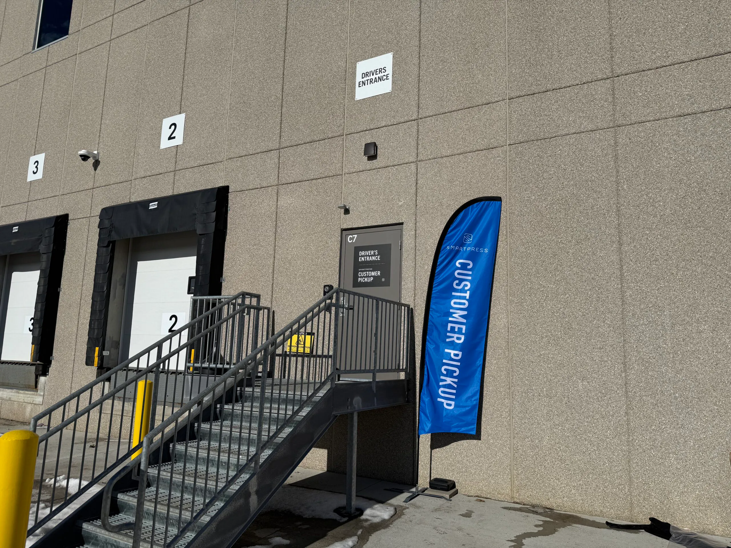 The customer pickup door at Smartpress with a blue feather flag next to it.