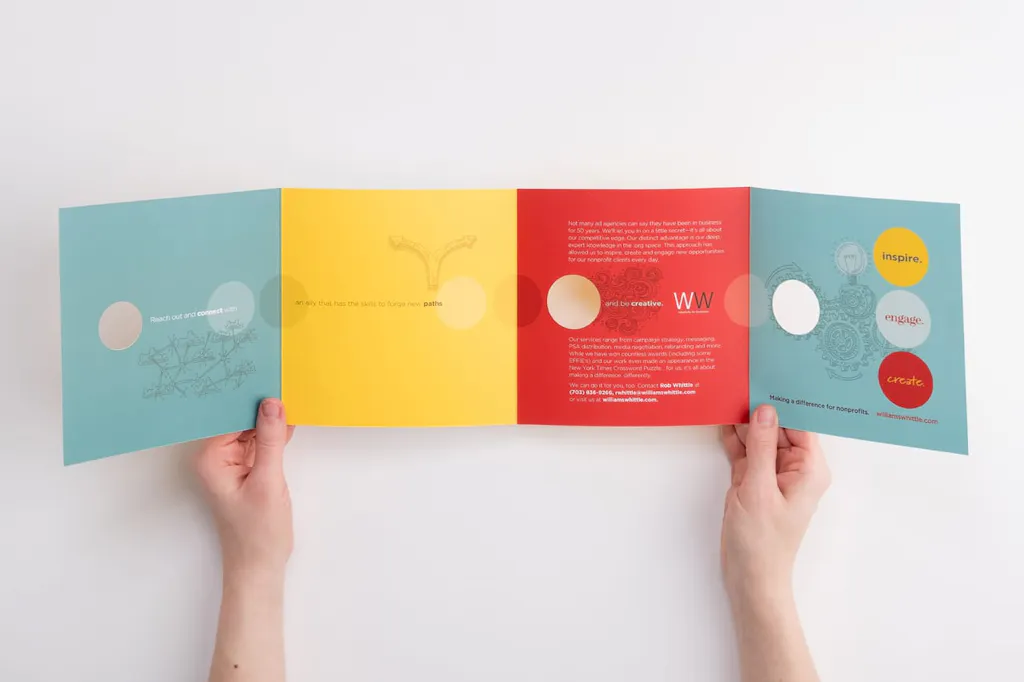 Two hands holding open a square brochure with four panels in blue, yellow and red.
