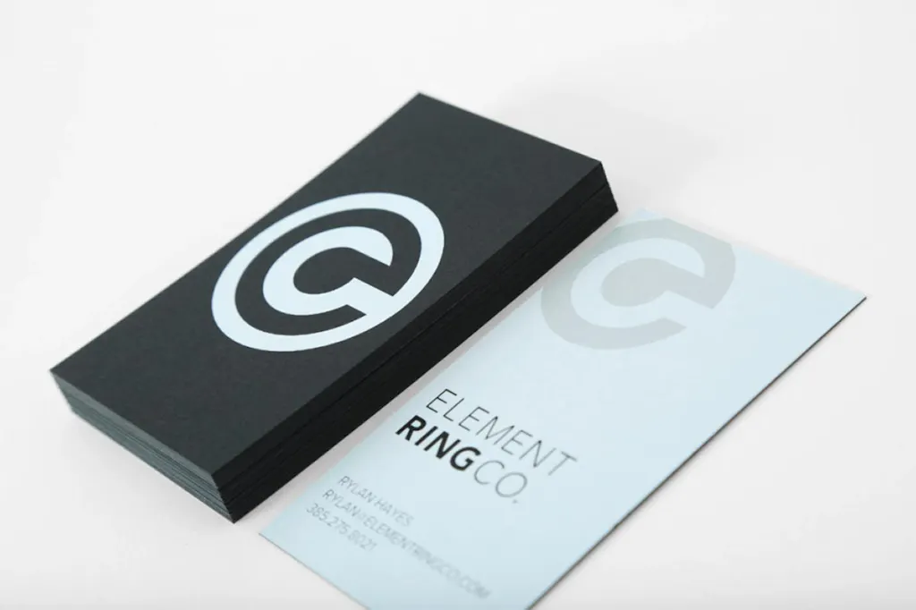 A stack of business cards with a black design and white ink printing next to another business card with Element Ring Co.