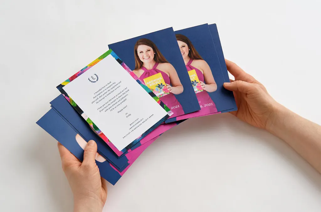 Two hands holding fanned-out custom postcards with a woman in a pink dress on the front and text on the back.