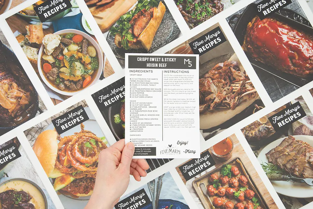 A hand holding a recipe card printed on a postcard above more recipe cards lined up in rows.