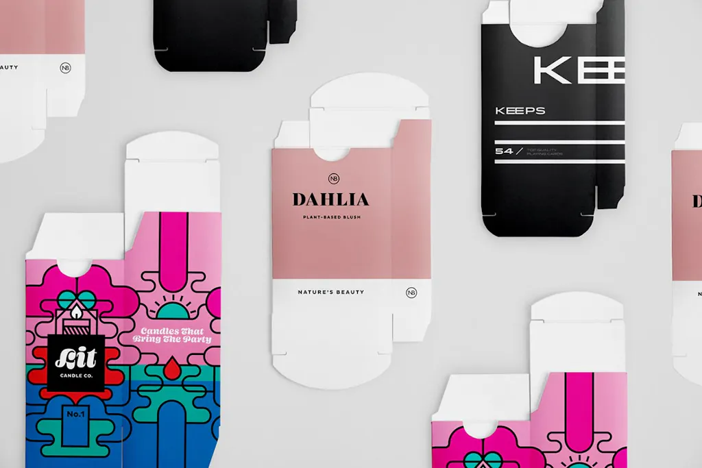 Custom tuck boxes laying flat with various designs in black, pink, green and blue.