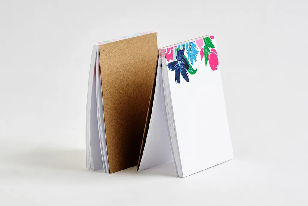 Two custom notepads with one showing the chipboard back and one showing a floral design on the front. 