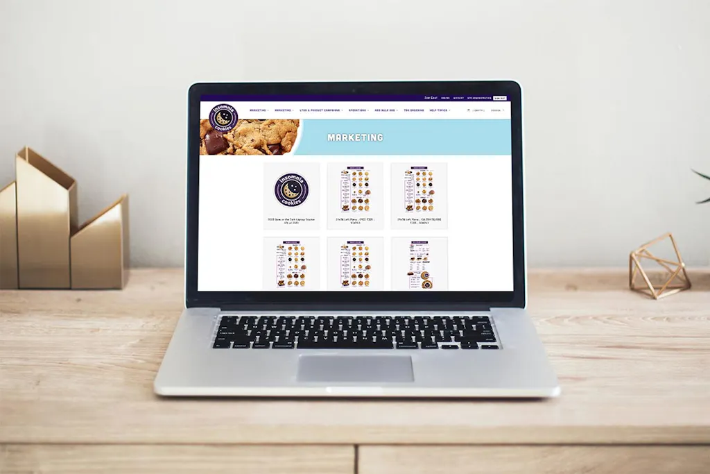 A laptop sitting on a wooden desk showing the Smartpress Storefront for Insomnia Cookies.