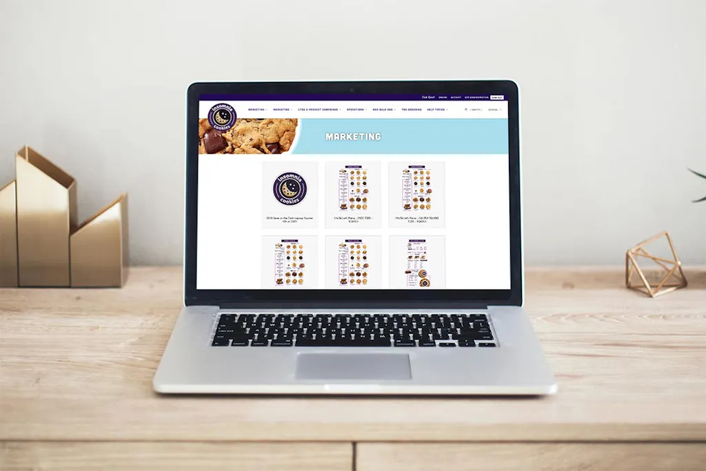 A laptop sitting on a wooden desk showing the Marketing on Demand platform for Insomnia Cookies.