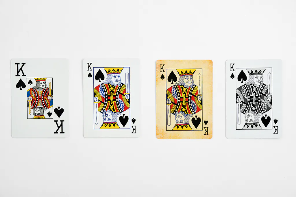 Four King playing cards lined up in a row with different face designs, including enlarged letters and a vintage background.
